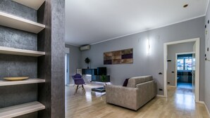 A modern living room with a sofa, a coffee table, and a TV. There are shelves and a plant. - Family Apartments Verdi (Trento)