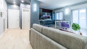 A modern living room with a sofa, a dining table with chairs, and a kitchen area in the background. - Family Apartments Verdi (Trento)