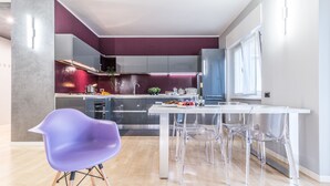 A modern kitchen with a dining area, featuring a purple chair, clear chairs, and a white table. - Family Apartments Verdi (Trento)