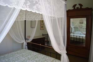 A bedroom with a bed, a wooden desk, a chair, and a window with a metal railing.