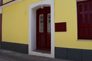 A yellow building with a red door and a small window with shutters.