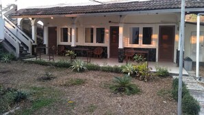 A covered outdoor seating area with tables and chairs, a staircase leading to an upper level, and a garden with various plants. - Bunga Ayu Seaside Resort (Pelabuhan Ratu)