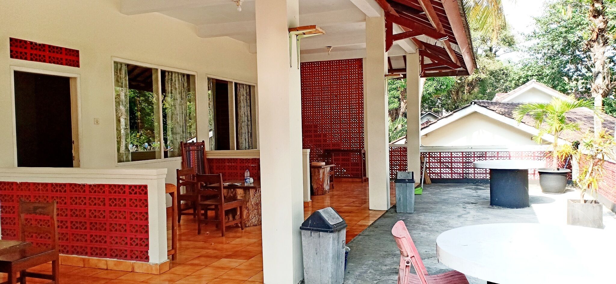 A covered outdoor area with a dining table and chairs, a trash bin, and a red decorative screen.