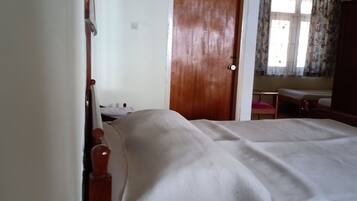 Una habitación con cama, una puerta de madera, una mesita y una ventana con cortinas.