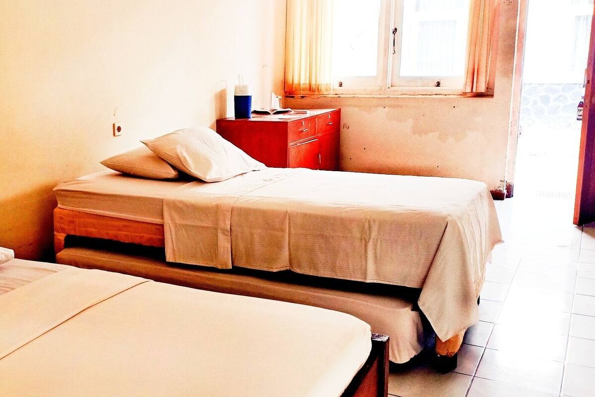 A room with two beds, a red dresser, and a window with curtains.