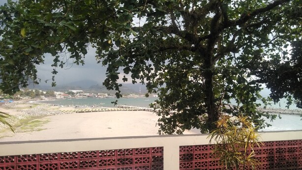 A beach view with a white table and a potted plant, overlooking a sandy shore and a marina with boats. - Bunga Ayu Seaside Resort (Pelabuhan Ratu)