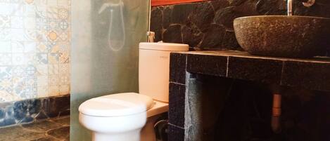 A bathroom with a toilet, a stone sink, and a shower.