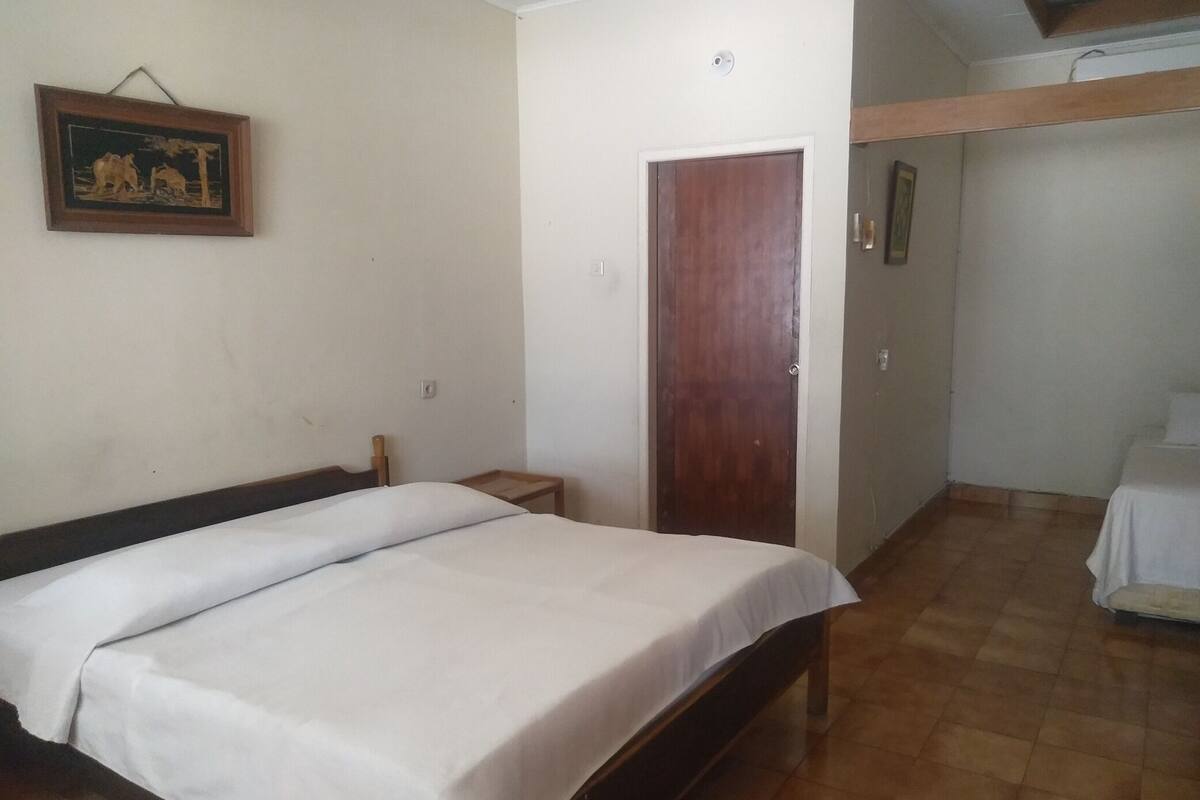 A bedroom with a bed, a wooden door, a small bedside table, and a wall-mounted picture.