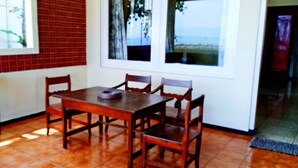 A dining area with a wooden table and chairs, a window with a view, and a tiled floor. - Bunga Ayu Seaside Resort (Pelabuhan Ratu)