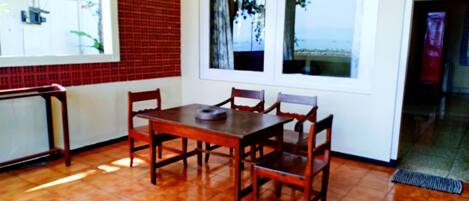 A dining area with a wooden table and chairs, a window with a view, and a tiled floor.
