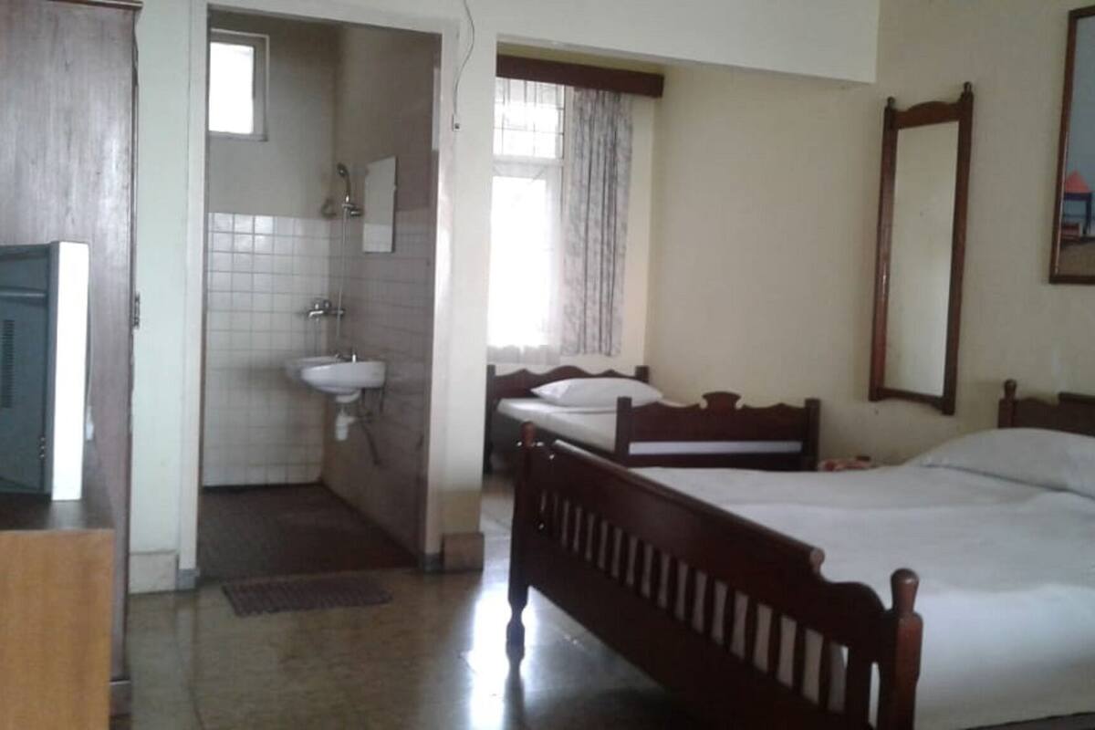 A bedroom with two single beds, a wooden headboard, a large mirror, and a bathroom with a sink and shower.