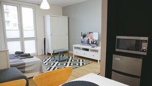 Un salon moderne comprenant un canapé, une table à manger, un téléviseur et un coin cuisine avec un four à micro-ondes.