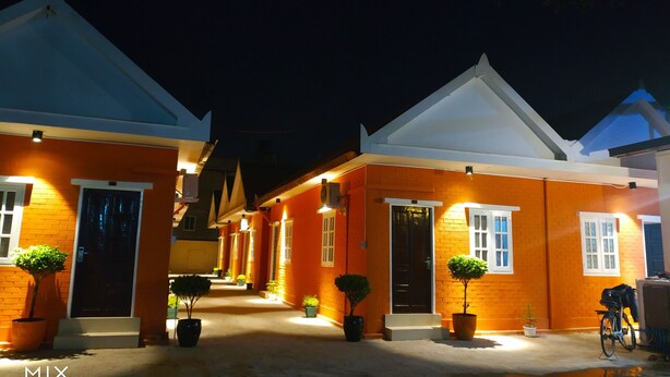 A row of orange-brick buildings with white trim and pitched roofs, each with a door and windows, and potted plants in front. - Sunrise Square Motel (Yangon)