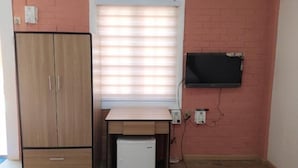 A room with a wooden wardrobe, a small white refrigerator, a desk with a computer monitor, and a window with blinds. - Sunrise Square Motel (Yangon)