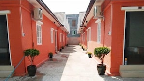A corridor with red brick walls, potted plants, and air conditioning units. - Sunrise Square Motel (Yangon)