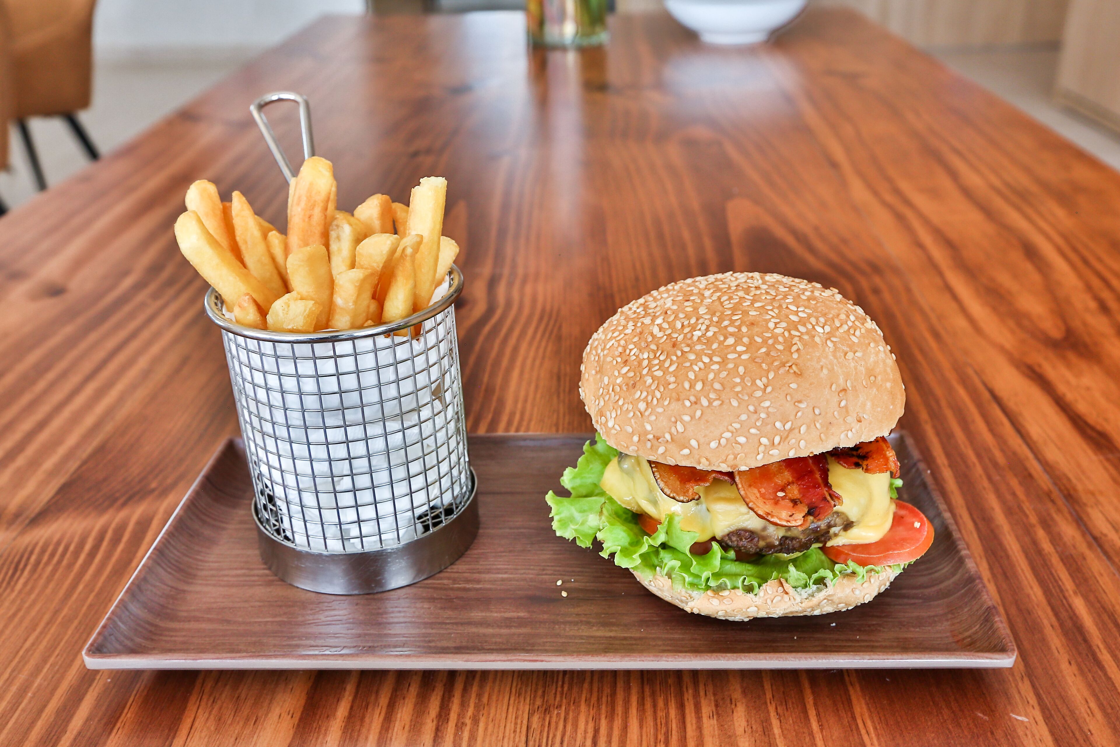 Une table en bois avec un panier en métal rempli de frites et un hamburger garni de laitue, de tomates et de fromage.