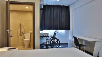 A hotel room with a wheelchair, a desk, and a toilet.