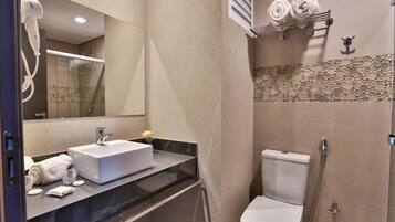 A modern bathroom with a white sink, mirror, and toilet. There are towels and toiletries on the counter.