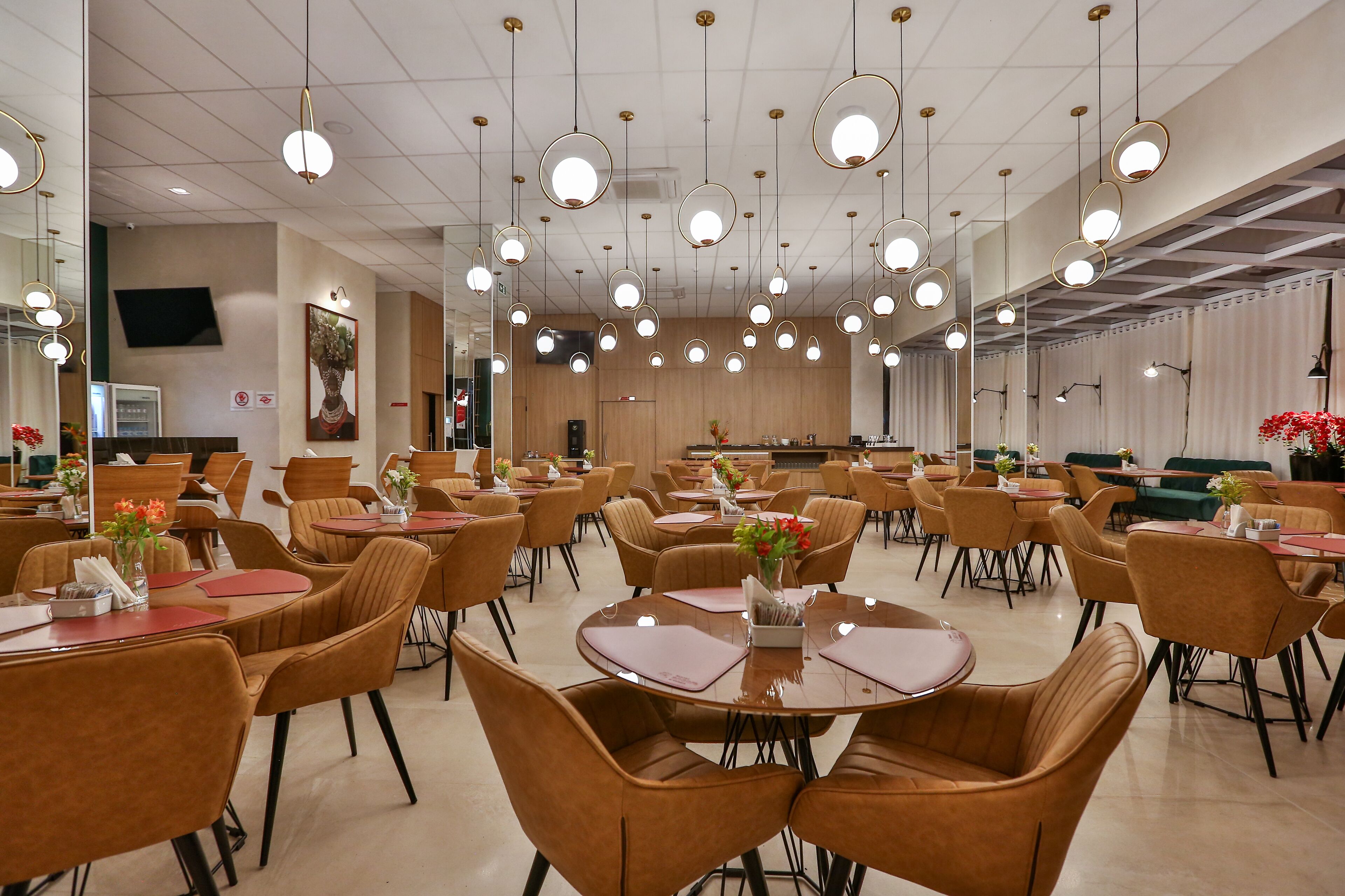 A spacious dining area with round tables and chairs, overhead lighting, and a neutral color palette.