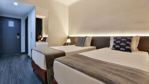 Ett hotellrum med två sängar, ett nattduksbord med en lampa, en spegel och en dörr.