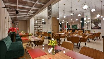 Un restaurante moderno con mesas de madera y sofás verdes, lámparas colgantes y un espejo grande en la pared.