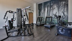 Ett gym med olika typer av träningsutrustning, inklusive löpband, en crosstrainer och styrketräningsmaskiner.