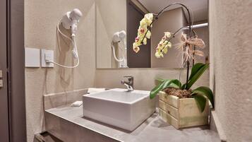 Een badkamer met een witte wastafel, een haardroger, een spiegel en een orchidee in een pot.