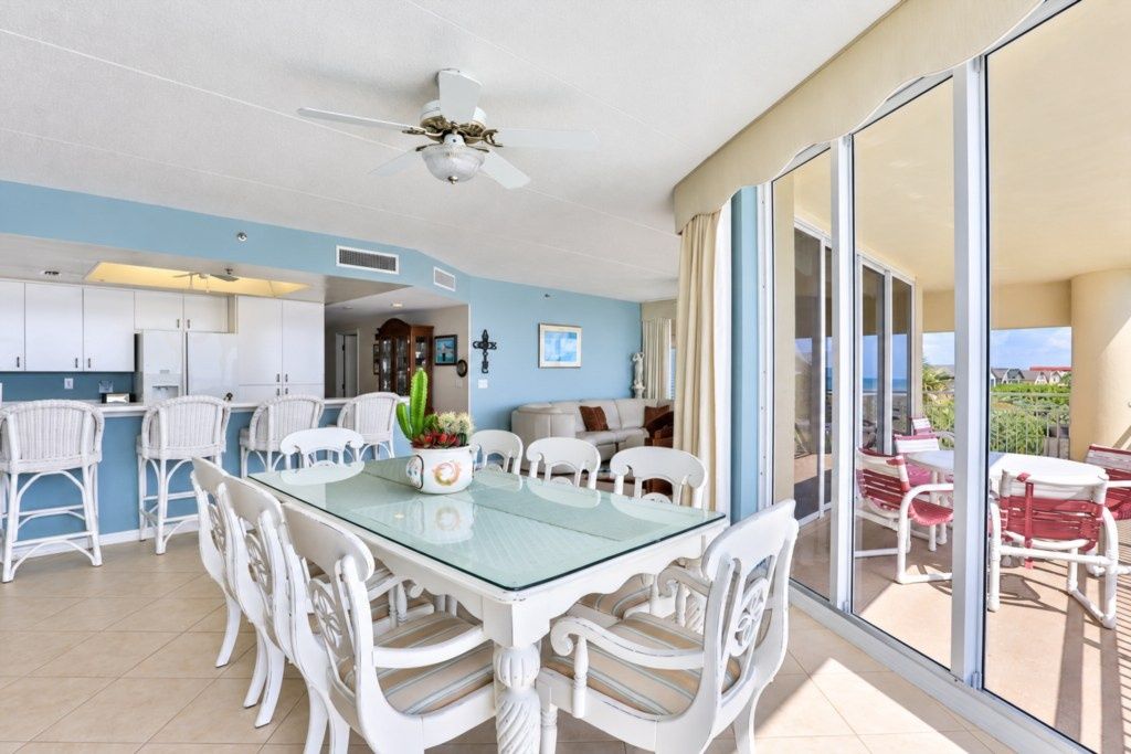 A modern kitchen with white cabinets, a glass dining table, and white wicker chairs.