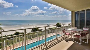 Ein Balkon mit Pool, Stühlen und Tisch mit Blick auf Strand und Meer.