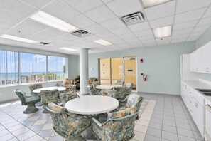 A room with a large window, a round table with chairs, and a kitchenette area. - Surf And Racquet 101 3 Bedroom Condo by RedAwning (New Smyrna Beach)