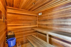 A sauna with wooden benches and a blue bucket. - Surf And Racquet 101 3 Bedroom Condo by RedAwning (New Smyrna Beach)