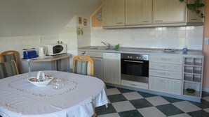 Eine kleine Küche mit Mikrowelle, Backofen und Spüle. Ein Esstisch mit weißer Tischdecke und einem Korb sind vorhanden. Die Küche hat helle Schränke und einen karierten Boden.