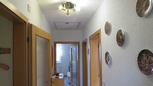 Ein schmaler Flur mit Holztüren, einer Deckenleuchte und Blick in einen Raum mit Toilette und Fenster.