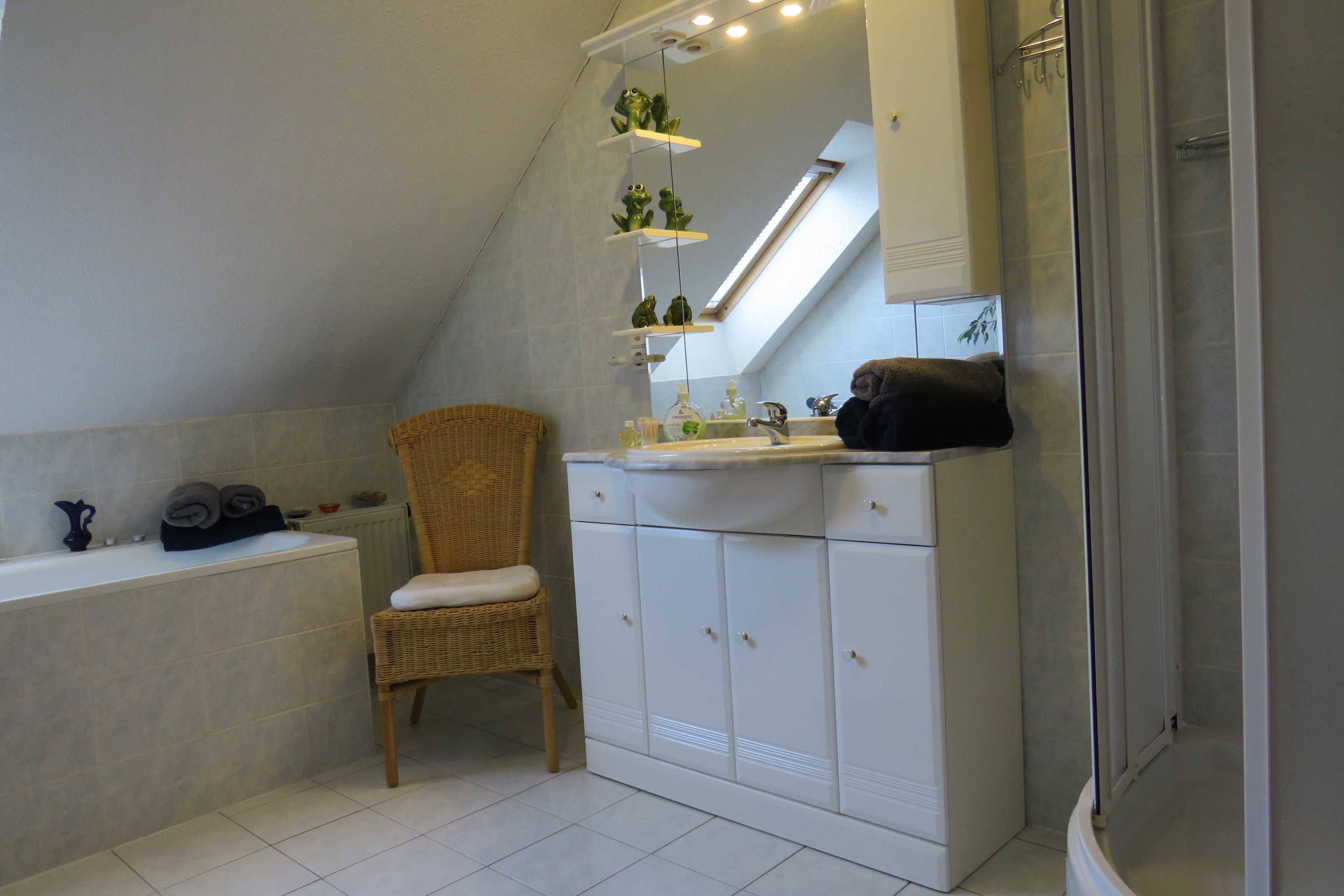 Ein Badezimmer mit einer Badewanne, einem Korbstuhl, einem Waschbecken mit Schränken und einer Duschkabine.