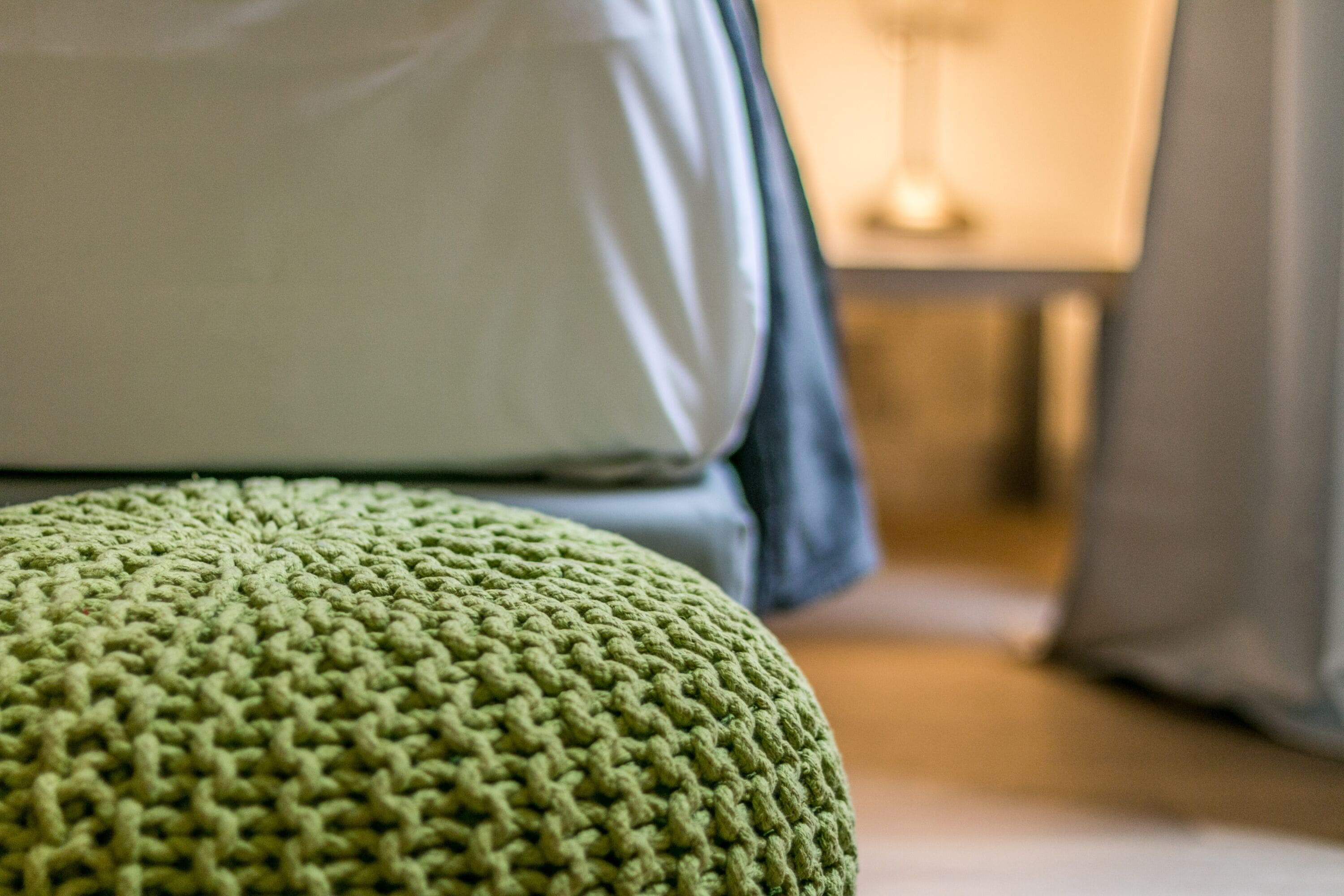 Primer plano de un reposapiés verde de punto y una almohada blanca en una habitación.
