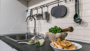 Una cocina con un lavamanos de acero inoxidable, un recipiente de vidrio con pasta, un bol de pan y un mortero con pilón.