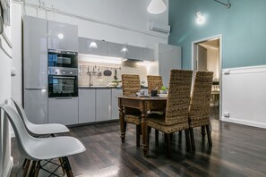 Eine moderne Küche mit weißen Schränken, einem eingebauten Ofen und einem Essbereich mit einem Holztisch und Korbstühlen.