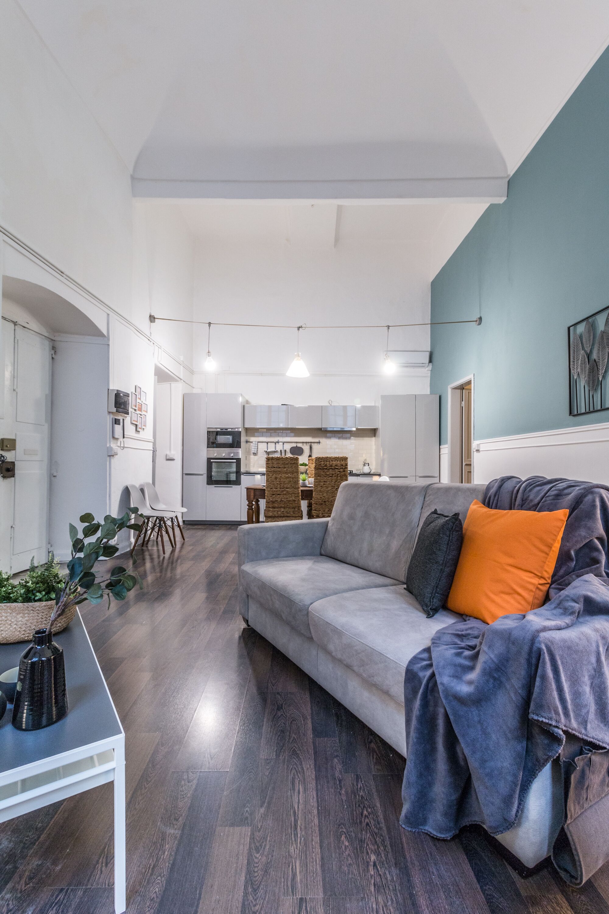 Een moderne woonkamer met een grijze bank, een kleine witte tafel en een donker houten vloer.