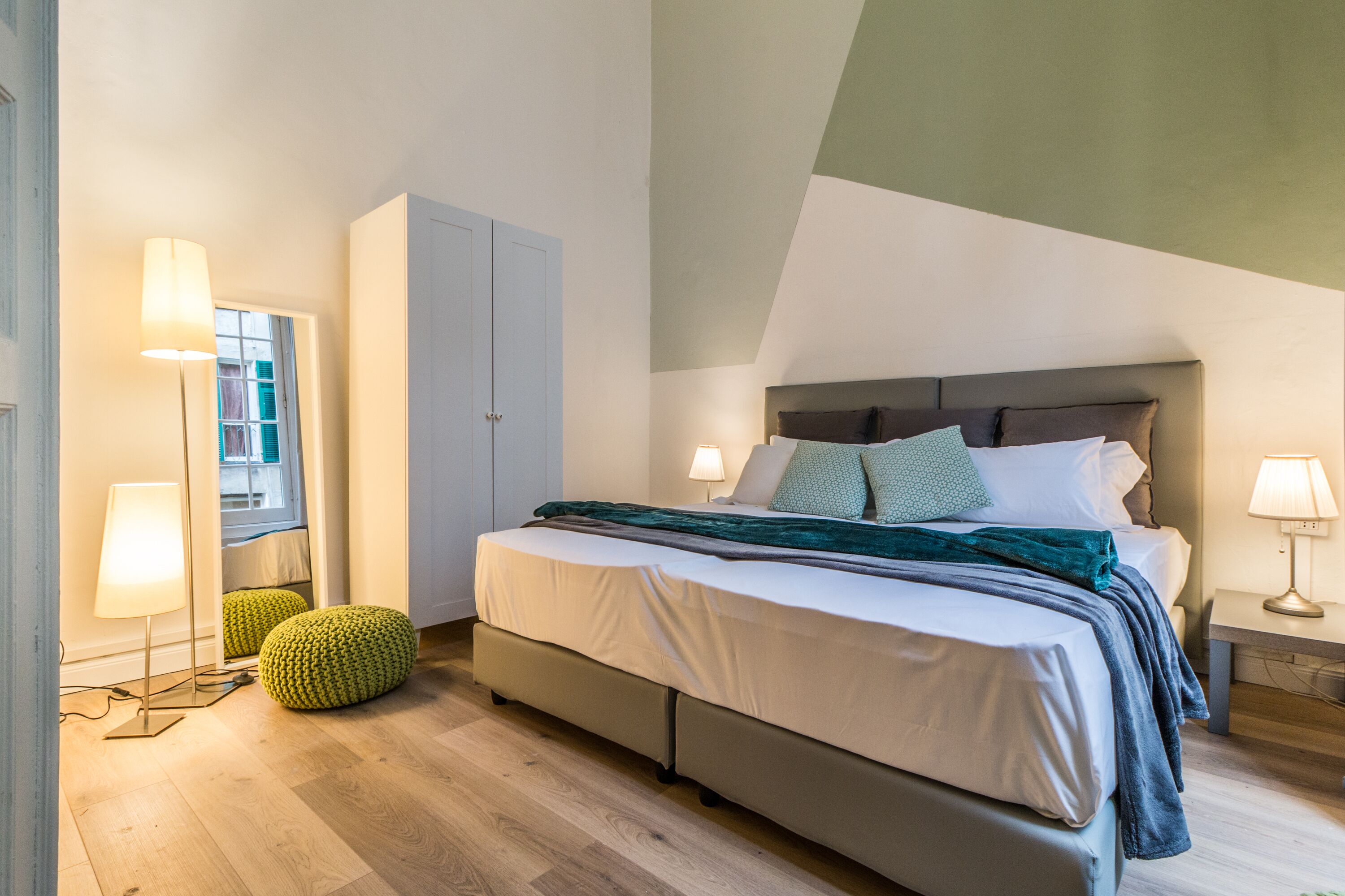 A bedroom with a bed, bedside lamps, a wardrobe, and a window.