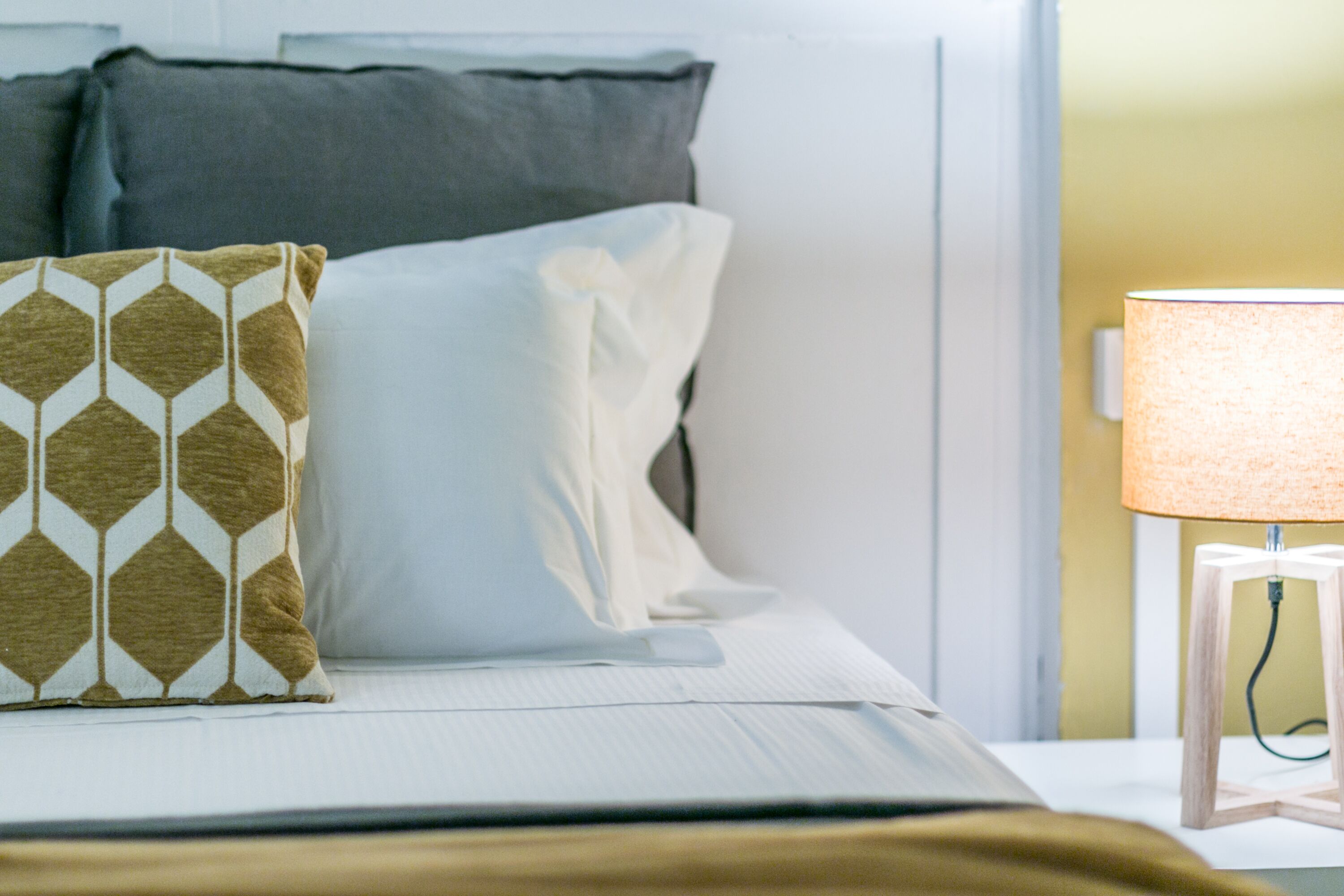 A neatly made bed with patterned pillows and a bedside lamp.
