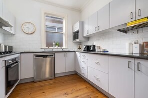 A modern kitchen with white cabinetry, stainless steel appliances, and a wooden floor.