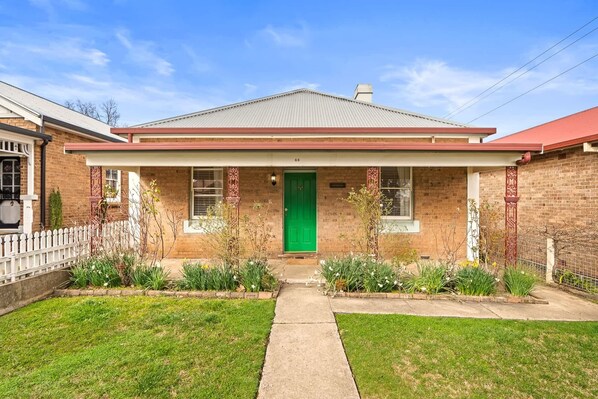 A two-story brick house with a green door, a front porch, and a small garden.
