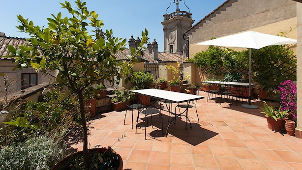 An outdoor patio with a table and chairs, surrounded by potted plants and a view of a church tower.