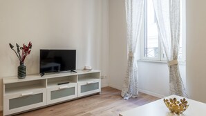 A modern living room with a flat-screen TV on a white TV stand, a vase with decorative items, and a white table with a decorative bowl. - Via degli Avignonesi (Rome)