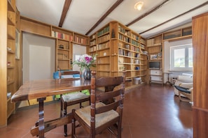 A spacious room with a large wooden table, chairs, and a bookshelf filled with books.
