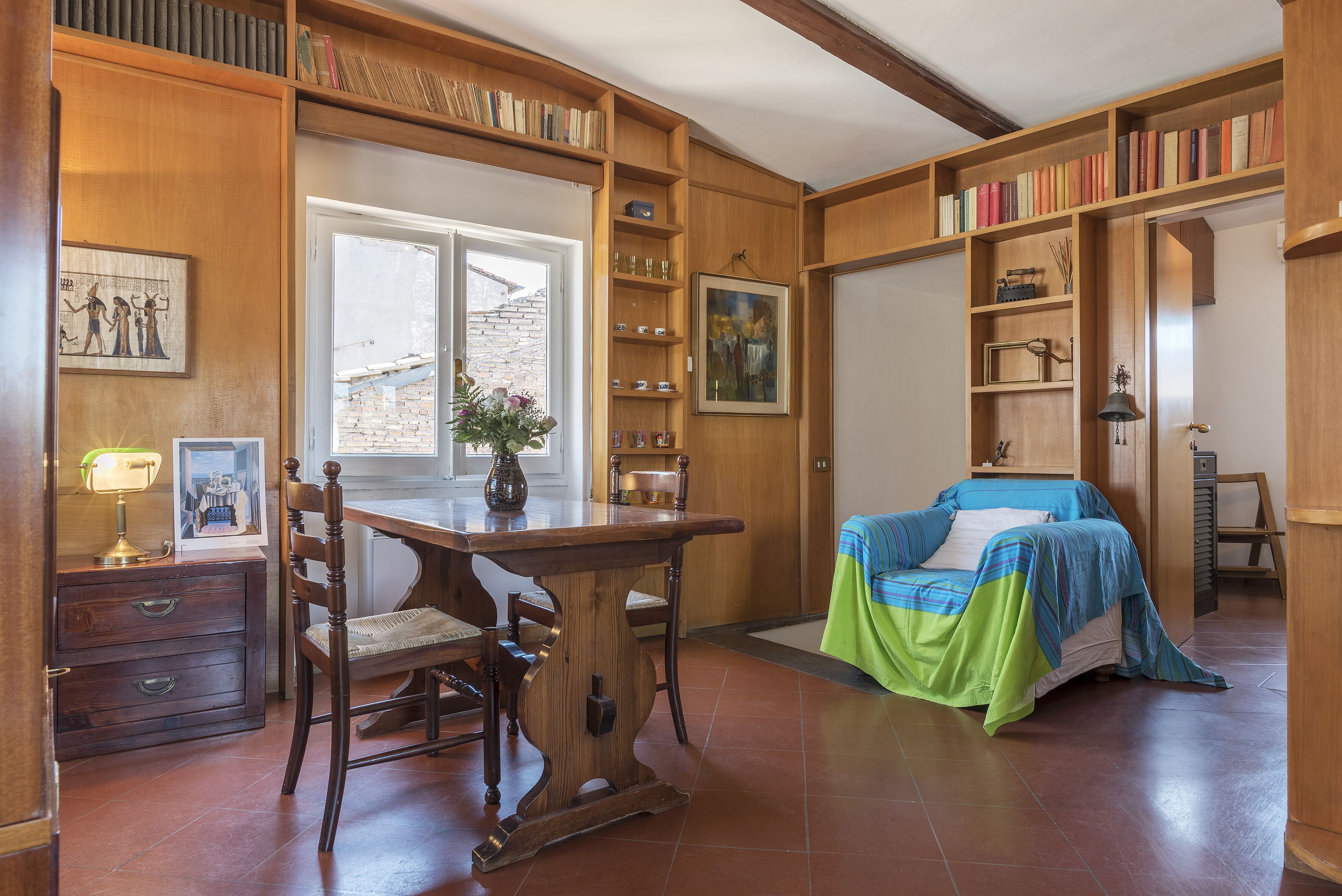Una habitación con un escritorio de madera, una silla y estanterías llenas de libros y objetos decorativos.