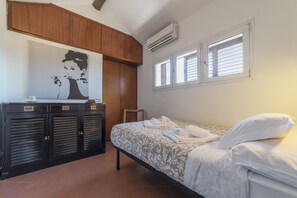 A bedroom with a bed, a wardrobe, a painting, and two windows.