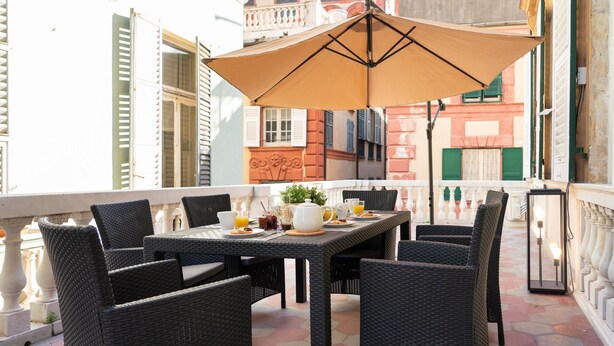 A balcony with wicker furniture, a table set with breakfast, and a large umbrella. - Family Apartments Angeli (Genoa)