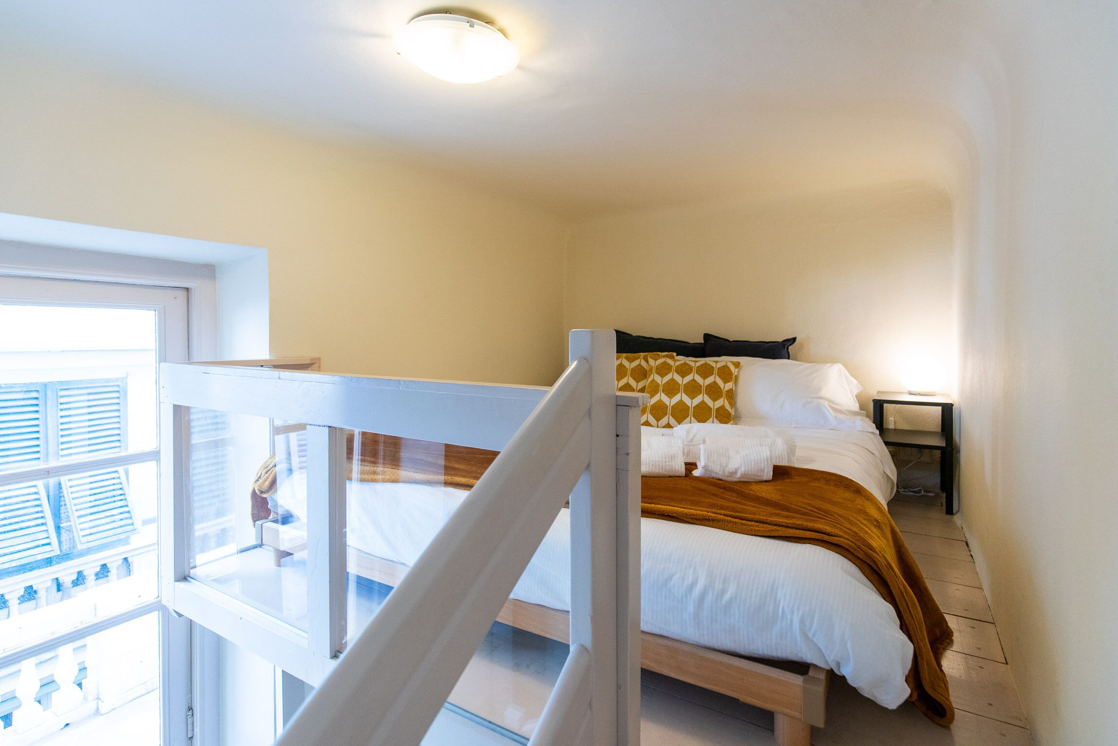 Une chambre à coucher avec un lit, une table de chevet, une fenêtre avec des stores et un balcon.
