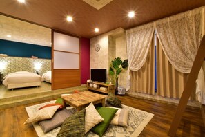 A modern hotel room with a wooden ceiling, a large bed, a TV, a wooden coffee table, and a view of the outside.